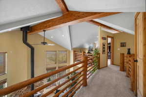 Loft space featuring exposed wood beams, vaulted ceilings with recessed lighting, and a wood-finish railing system overlooking the living area below