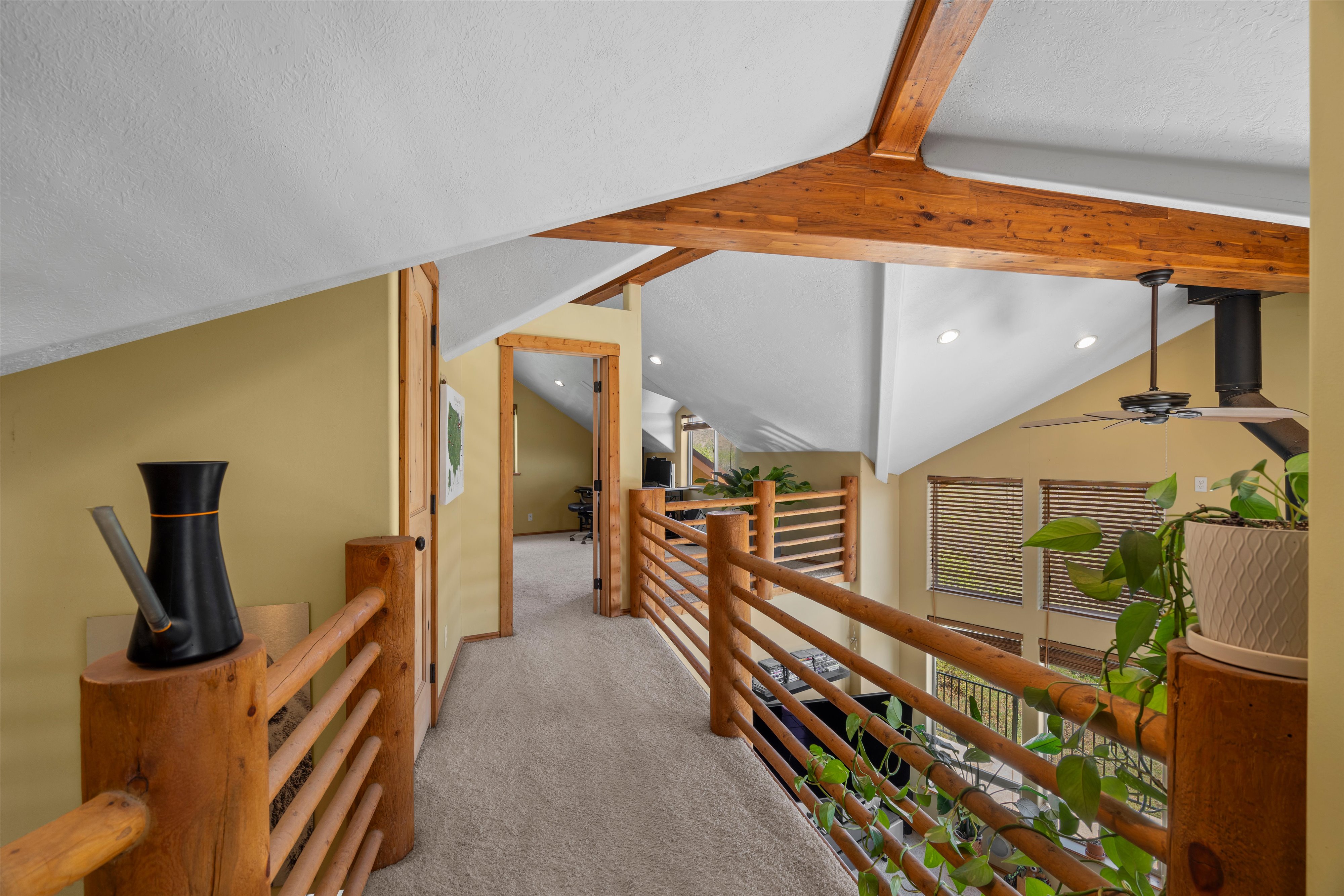 Expansive upper-level hallway featuring exposed wood beams, vaulted ceilings, recessed lighting, wood-finish railings, and neutral carpeting