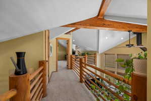 Expansive upper-level hallway featuring exposed wood beams, vaulted ceilings, recessed lighting, wood-finish railings, and neutral carpeting