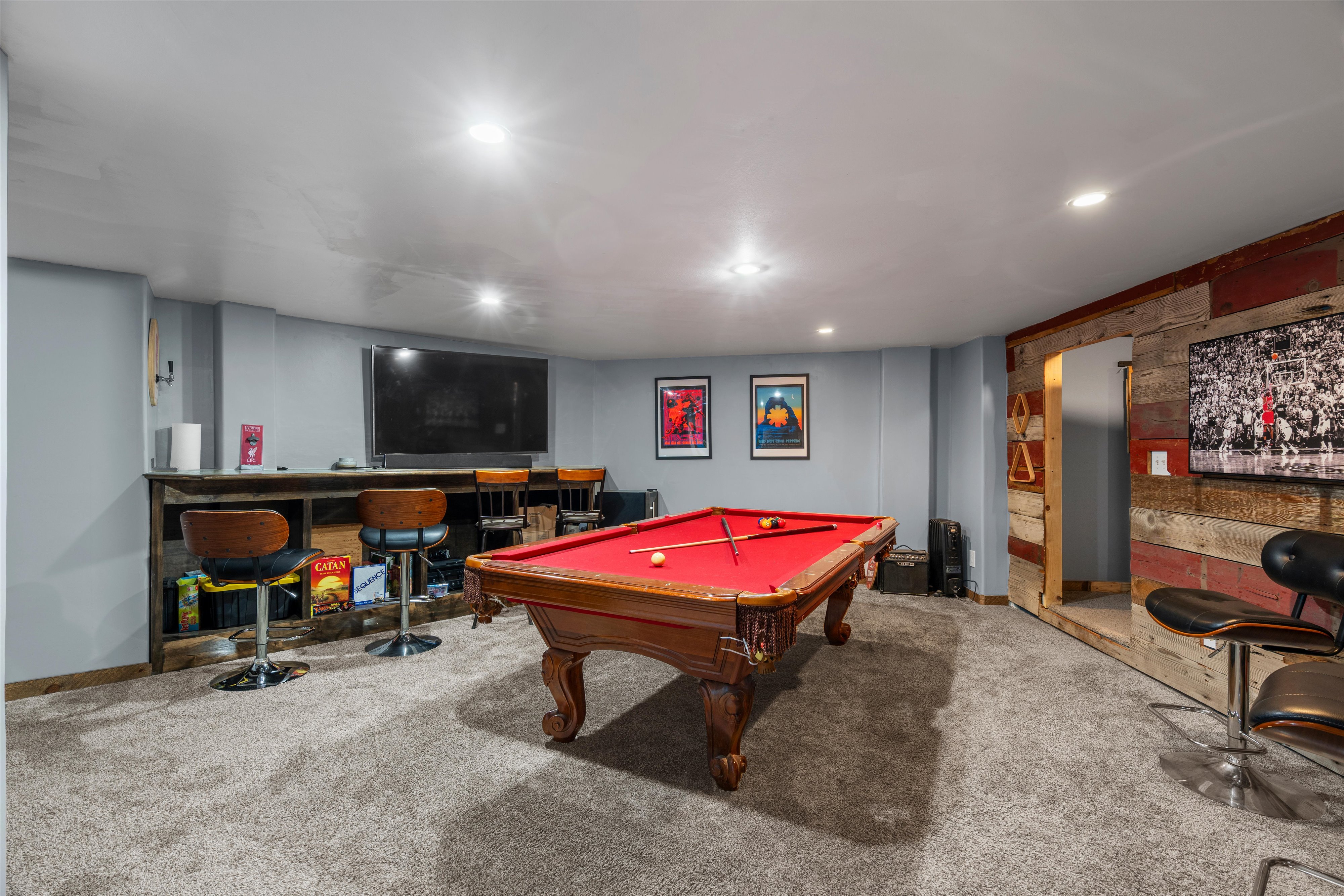Spacious entertainment room featuring recessed lighting, gray carpet flooring, a built-in bar with wood-finish paneling, and a rustic wood-finish accent wall