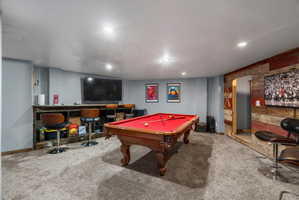 Spacious entertainment room featuring recessed lighting, gray carpet flooring, a built-in bar with wood-finish paneling, and a rustic wood-finish accent wall
