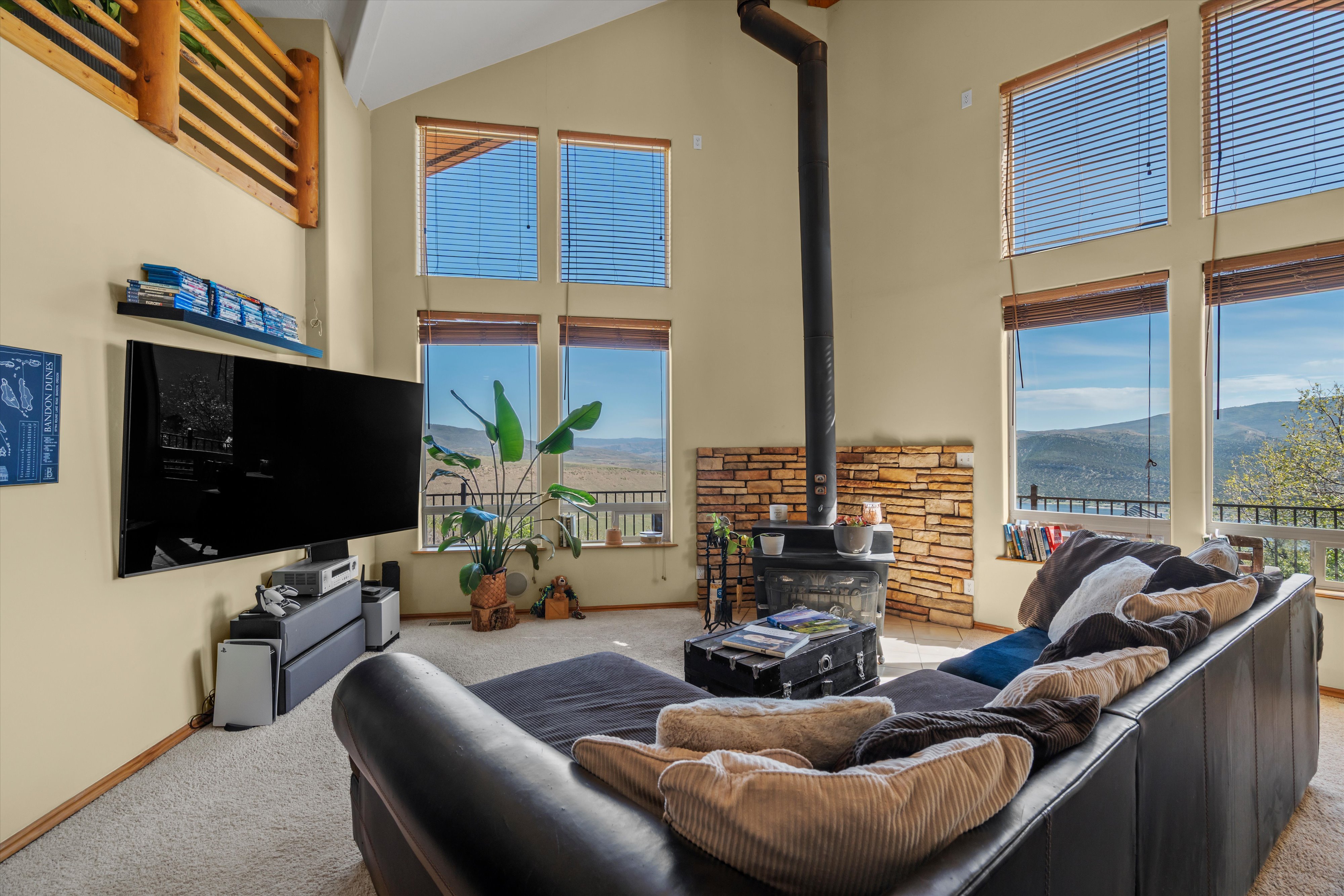 Great room featuring a vaulted ceiling, wood-burning stove with a stone surround, and multiple large windows with mountain scenery
