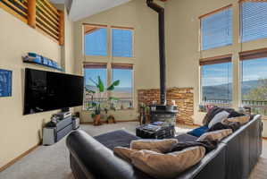 Great room featuring a vaulted ceiling, wood-burning stove with a stone surround, and multiple large windows with mountain scenery