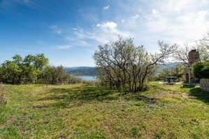 Expansive outdoor space featuring a stone fireplace, mature trees, horseshoe pit, and natural landscaping