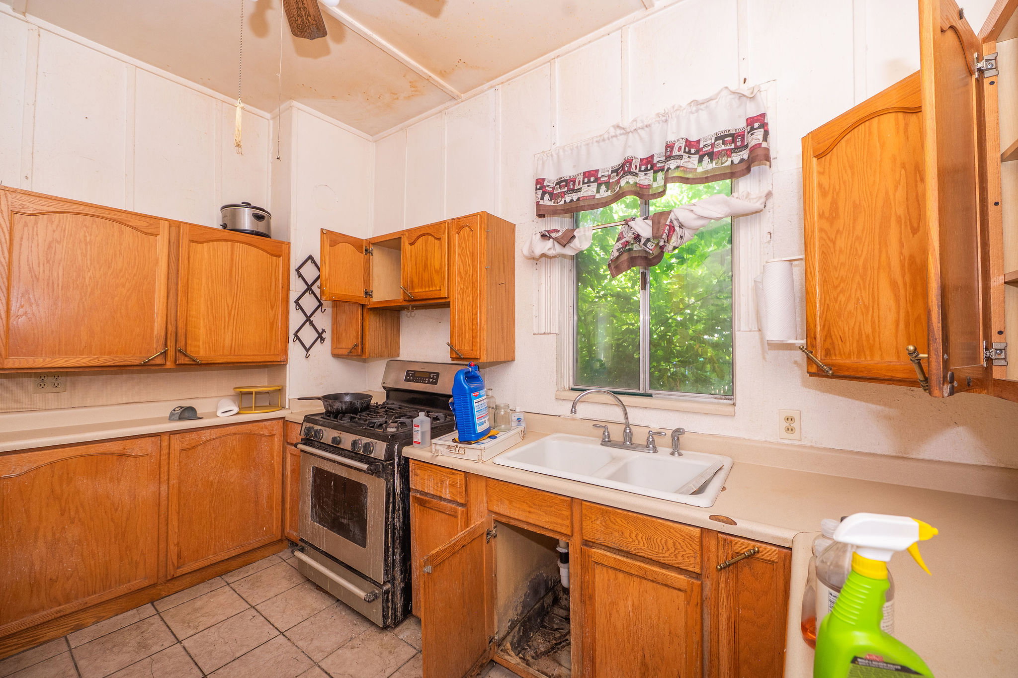 Galley kitchen featuring wood-finish cabinetry, a stainless steel range, and a double basin sink with a window above