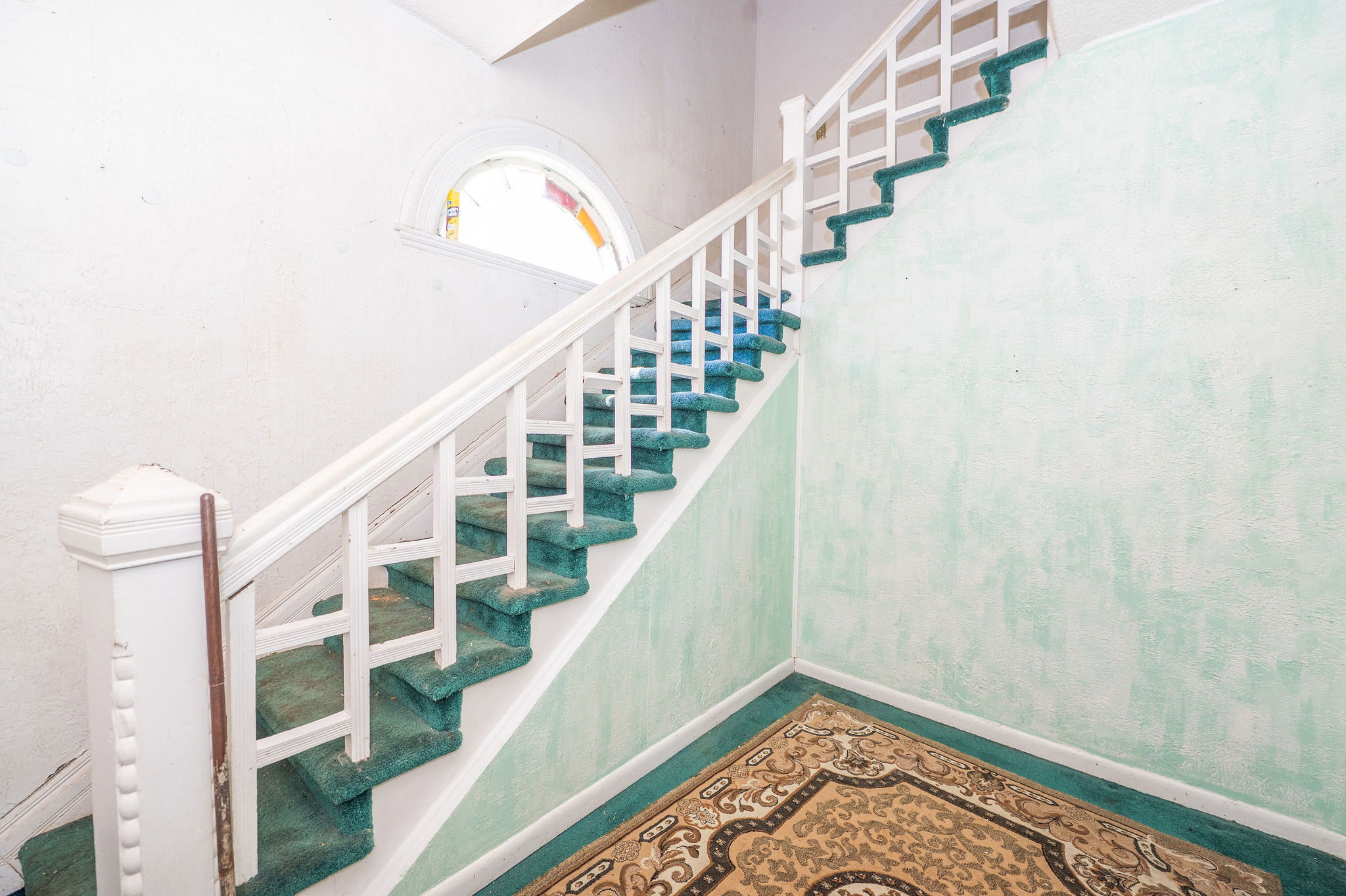 Staircase featuring white balusters and green carpeted treads, complemented by a stained glass arched window and textured wall finish