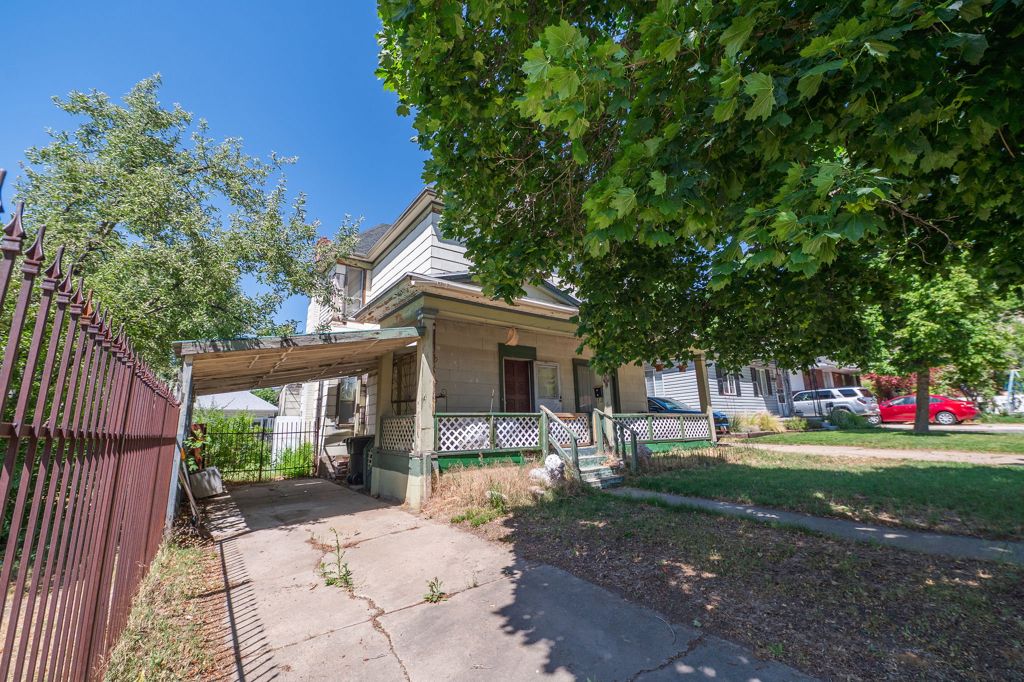 Two-story residence featuring a covered carport, front porch with lattice detailing, and mature trees providing natural shade