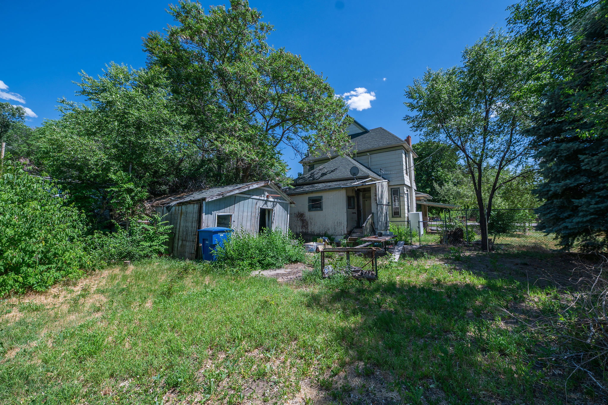 Exterior property featuring a two-story residence with a side porch, a detached storage shed, and mature trees