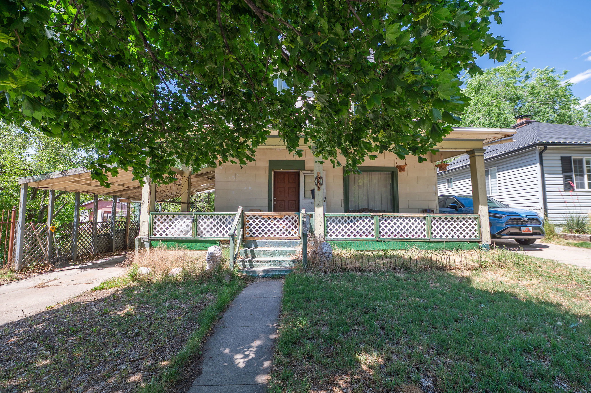 Single-story residence featuring a covered front porch with lattice railing, a paved driveway, and a covered carport