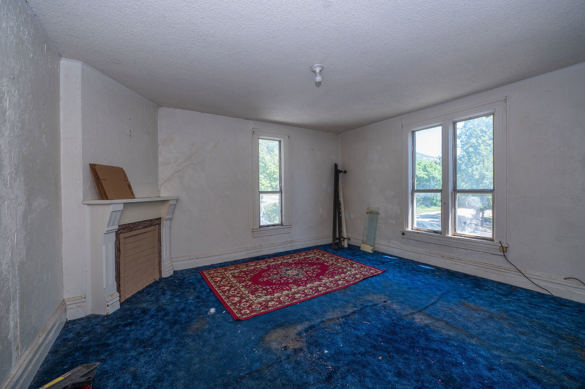 Interior space featuring a decorative fireplace mantel, two large windows, a single smaller window, and a ceiling-mounted light fixture