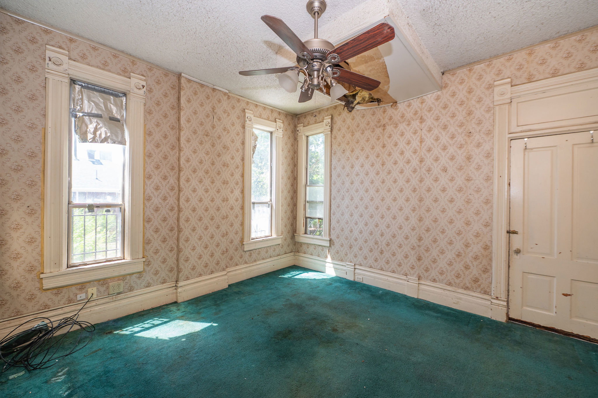 Room featuring patterned wallpaper, a ceiling fan with wood-finish blades, and teal carpeting