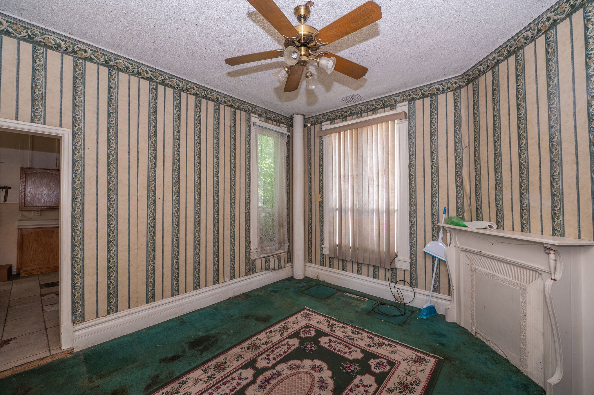 Room featuring patterned wallpaper, a ceiling fan with light fixture, and a decorative mantel