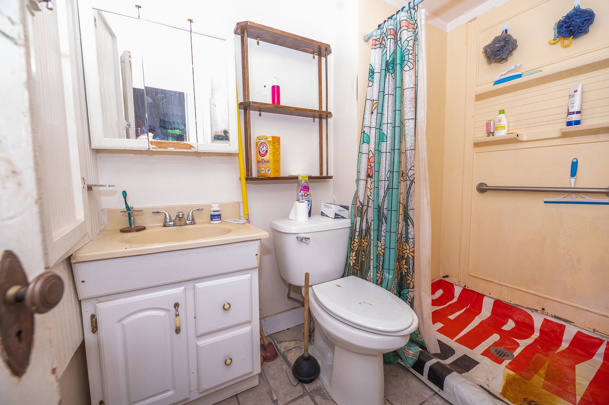Compact bathroom featuring a corner vanity with integrated sink, wall-mounted medicine cabinet, toilet, and shower area with grab bar