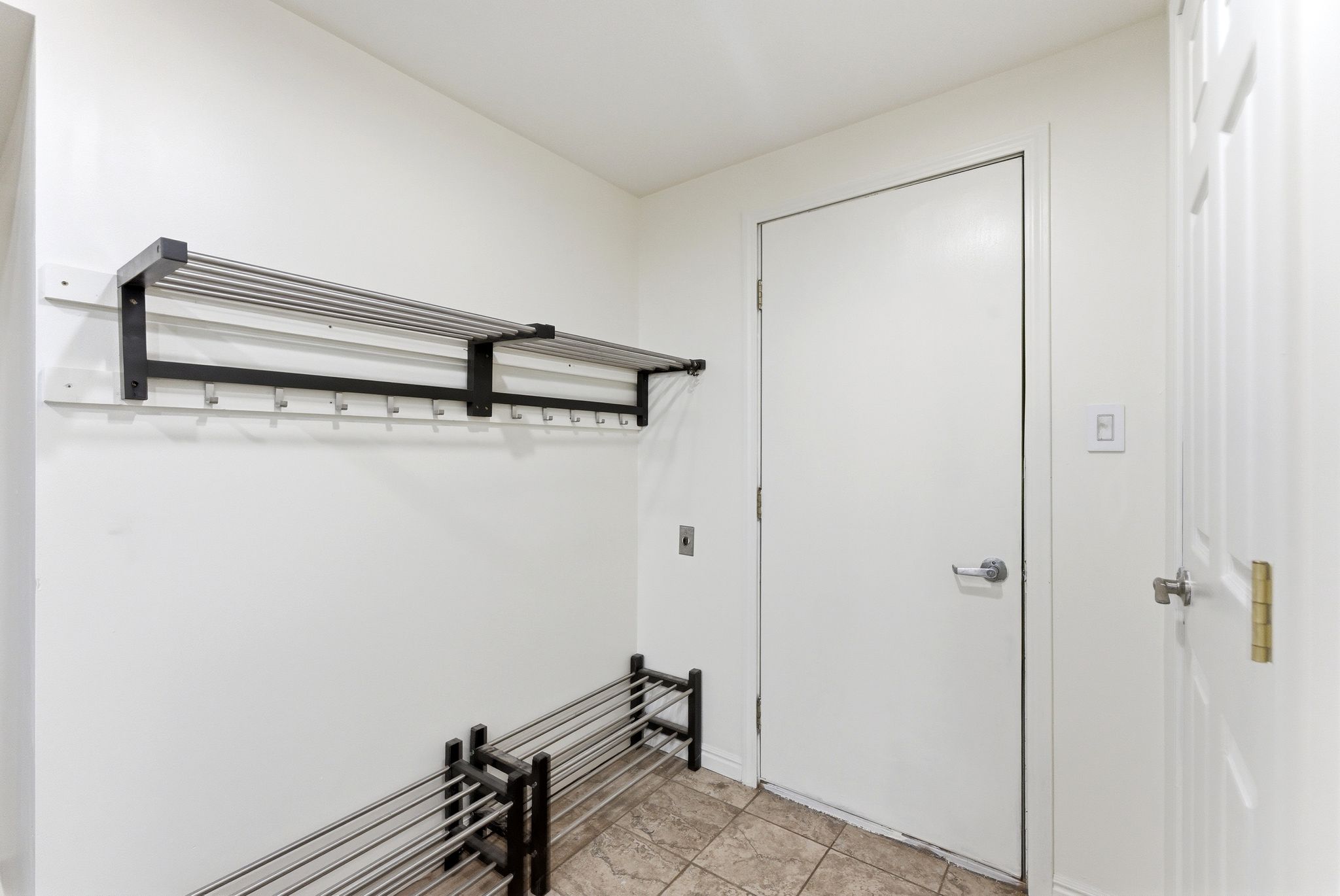 Tiled flooring entry space from garage with built-in wall-mounted coat rack and shoe rack