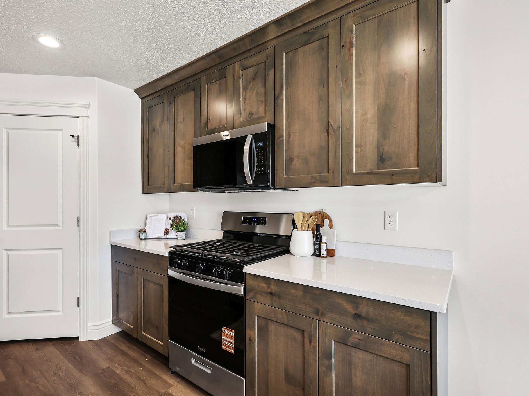 Kitchen area featuring dark wood-finish cabinetry, solid surface countertops, stainless steel gas range, and a built-in microwave