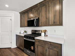 Kitchen area featuring dark wood-finish cabinetry, solid surface countertops, stainless steel gas range, and a built-in microwave