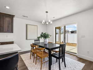 Dining area featuring wood-finish flooring, a contemporary chandelier, and a sliding glass door providing access to an outdoor patio