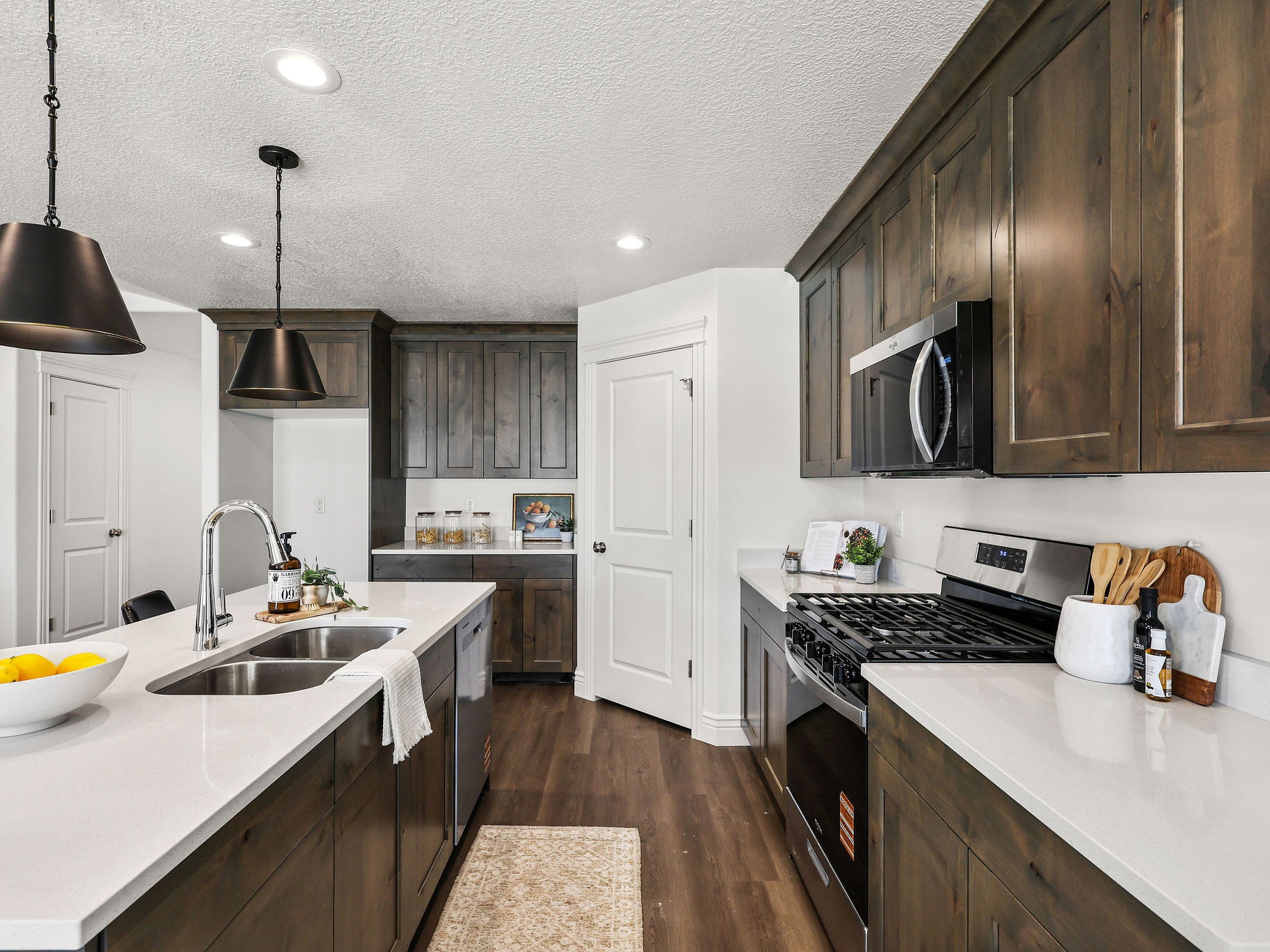 Kitchen featuring dark wood-finish cabinetry, stainless steel appliances, a center island with double sink, white countertops, and recessed lighting
