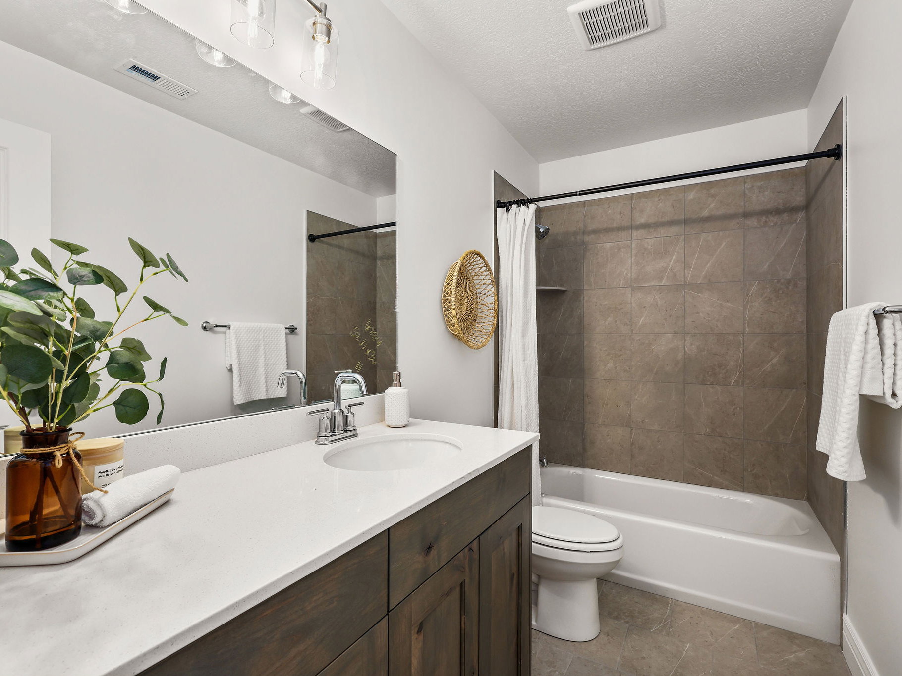 Full bathroom featuring a dark wood-finish vanity with an integrated sink and light-toned countertop, a large wall-mounted mirror, and a shower-over-tub combination with large format tiled surround