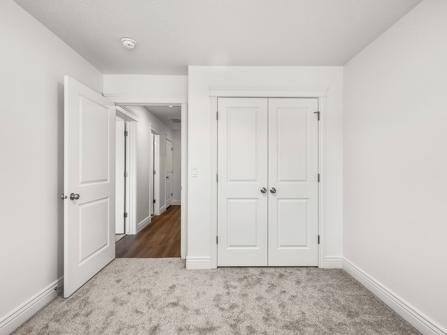 Carpeted room featuring a white paneled door, bi-fold closet doors, white baseboards, and a doorway opening to a hallway with wood-finish flooring