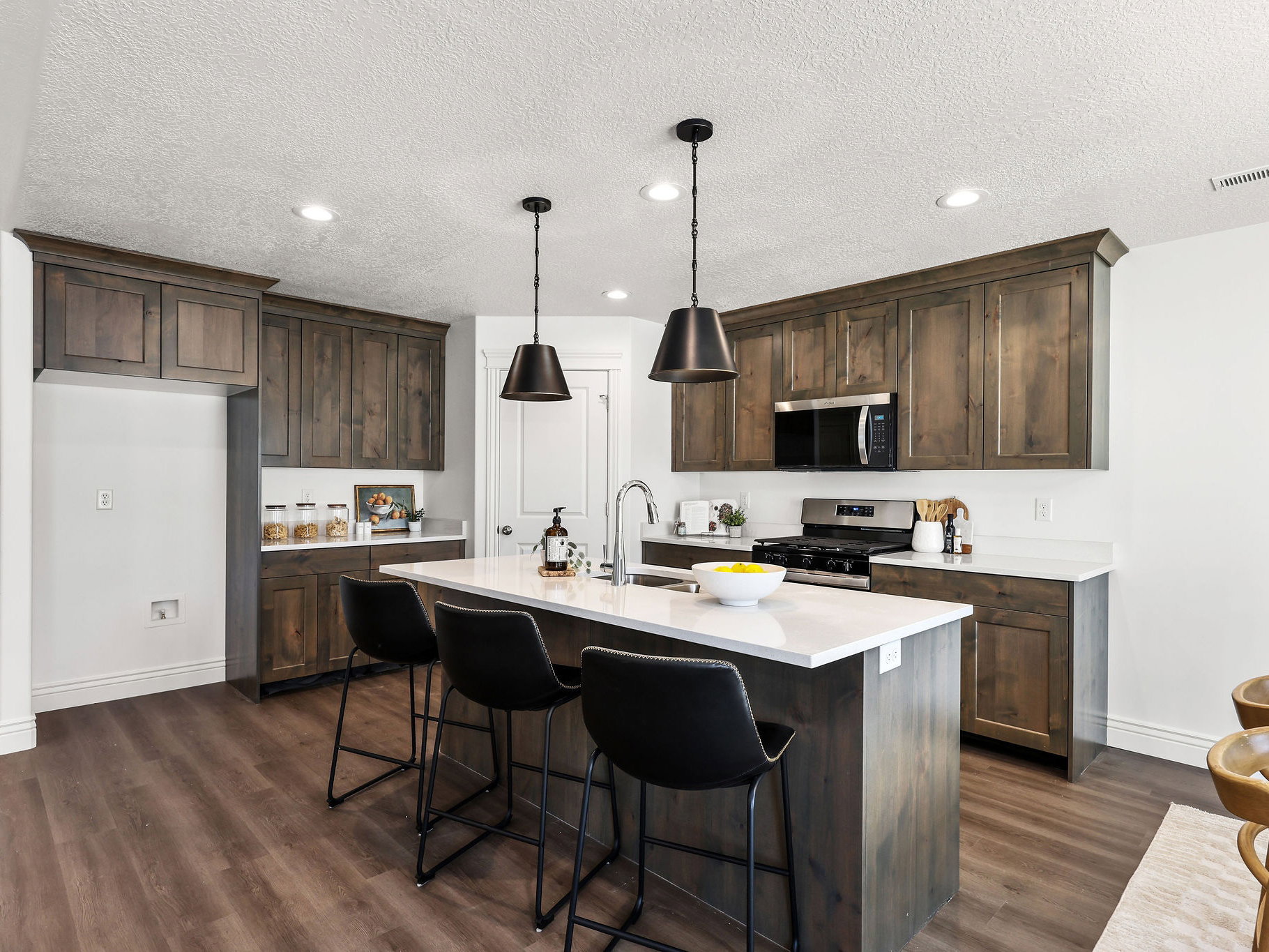Contemporary kitchen featuring dark wood-finish cabinetry, white countertops, and a central island with bar seating