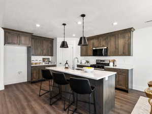 Contemporary kitchen featuring dark wood-finish cabinetry, white countertops, and a central island with bar seating