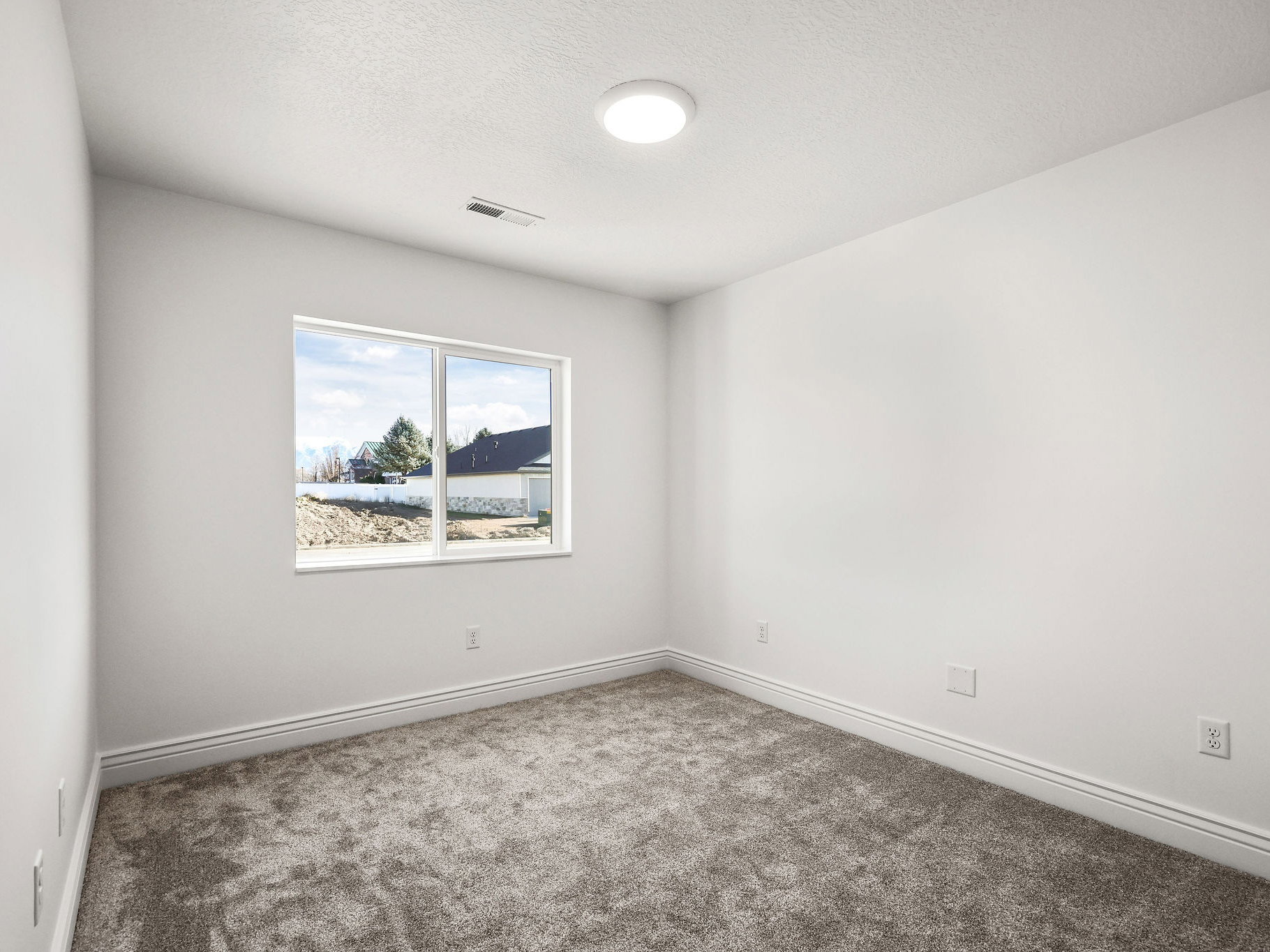 Bright room featuring a large double-pane window, flush-mount ceiling light fixture, grey carpet, white walls, and layered baseboards