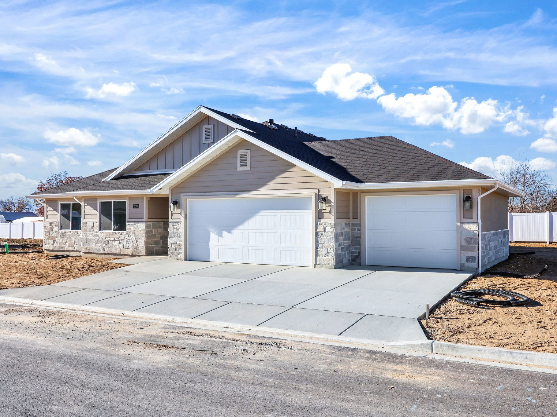 Contemporary-style residence featuring a two-car garage with white doors, light-toned horizontal siding, and stone veneer accents
