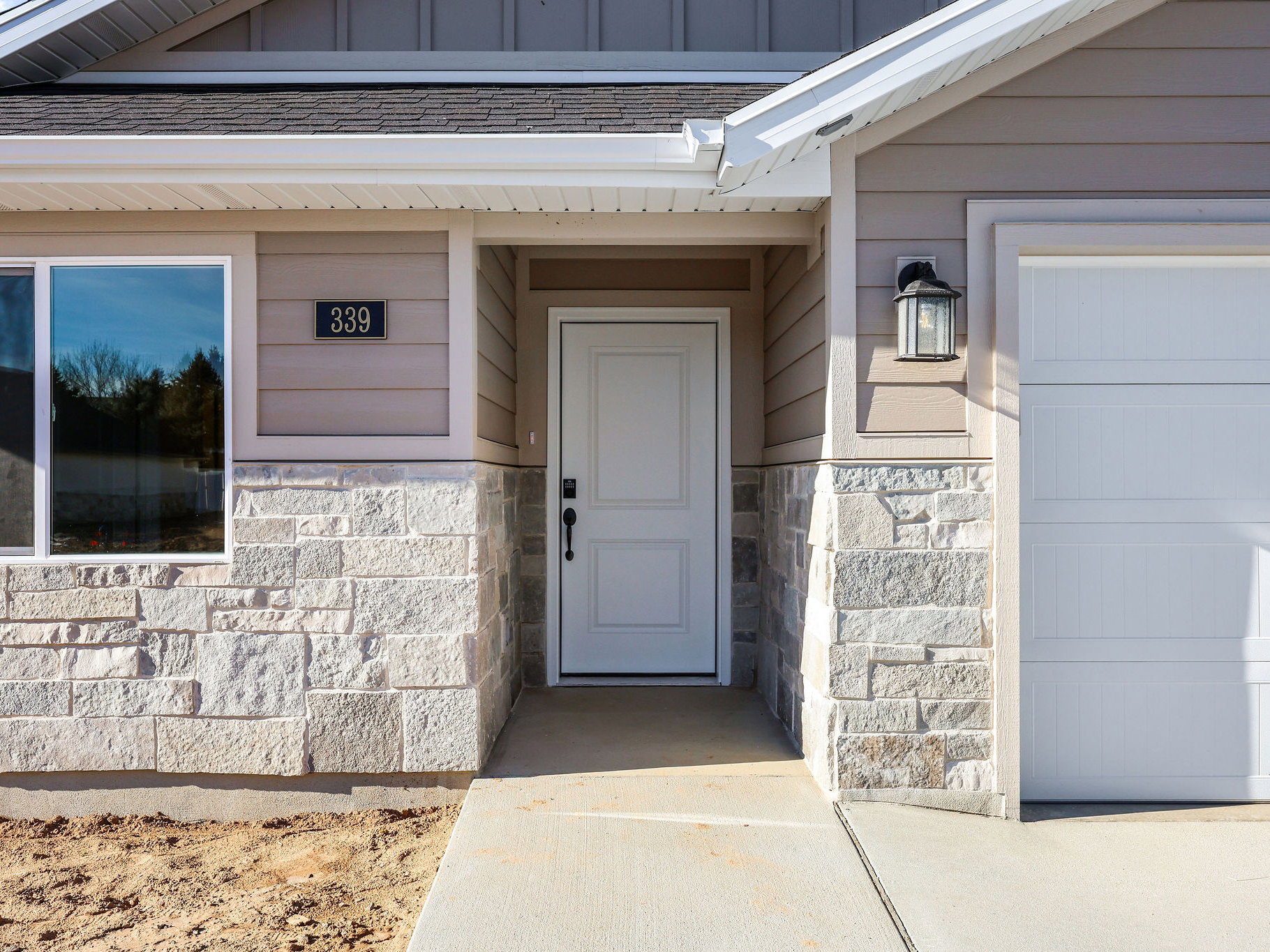 Inviting front entrance featuring a white panel door with black hardware, flanked by a concrete pathway and a white garage door