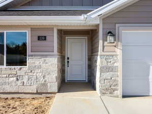 Inviting front entrance featuring a white panel door with black hardware, flanked by a concrete pathway and a white garage door