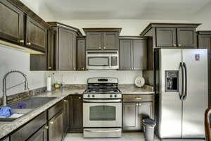 Kitchen featuring dark wood-finish cabinetry with gold-tone hardware, stainless steel appliances, a double basin sink with a high-arc faucet, and granite-look countertops