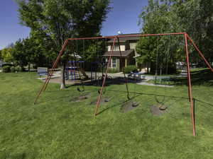 Expansive green space featuring a red swing set, a separate play structure with a slide, and mature trees