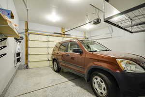 Attached garage featuring an epoxy-coated floor, overhead storage racks, an automatic garage door opener, and integrated wall shelving