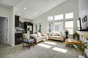Vaulted ceilings enhance this open-concept living area, featuring a wall of windows, recessed lighting, and soft carpeting