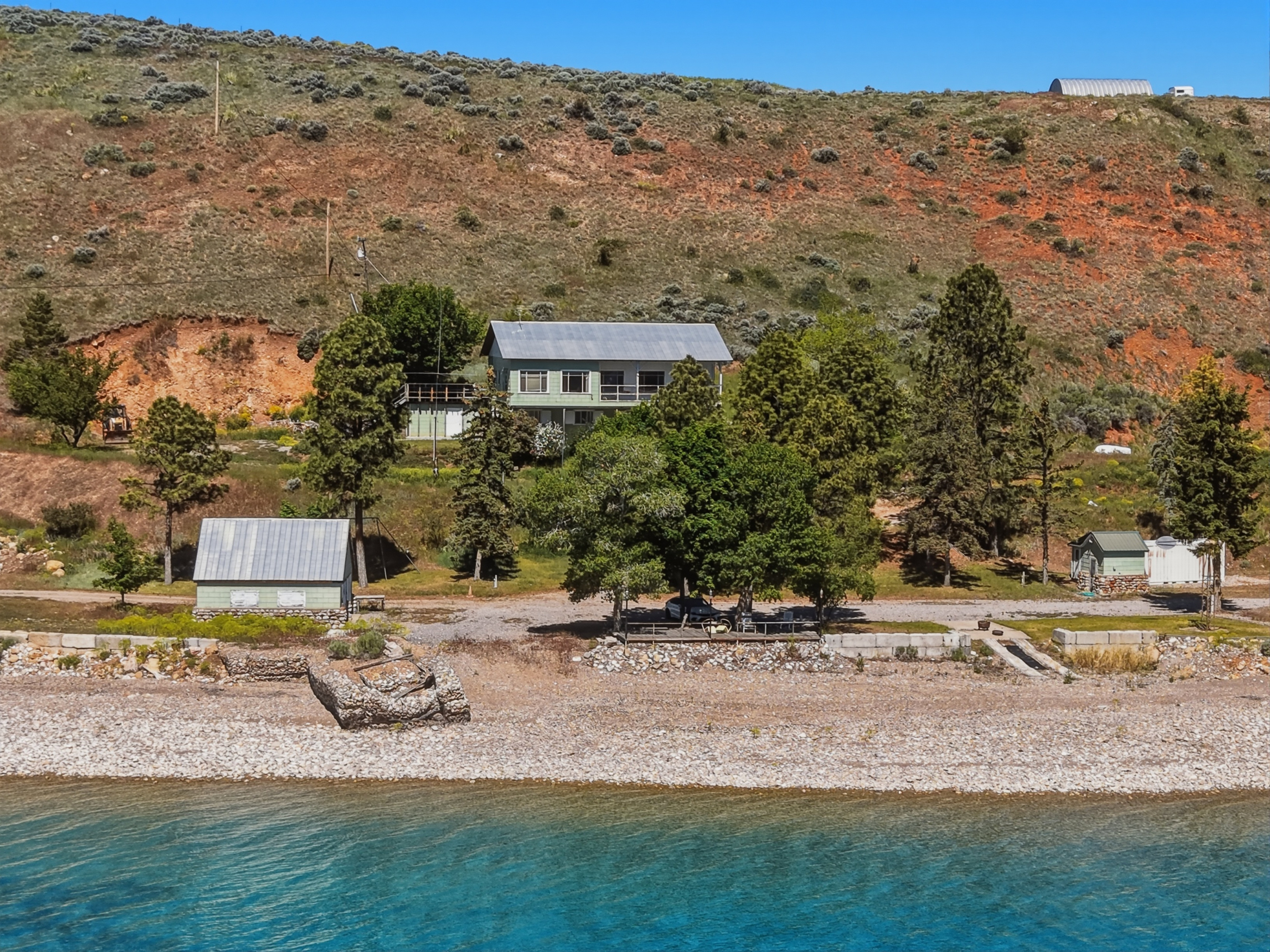 Lakeside property featuring a multi-level residence with light green siding and a grey roof