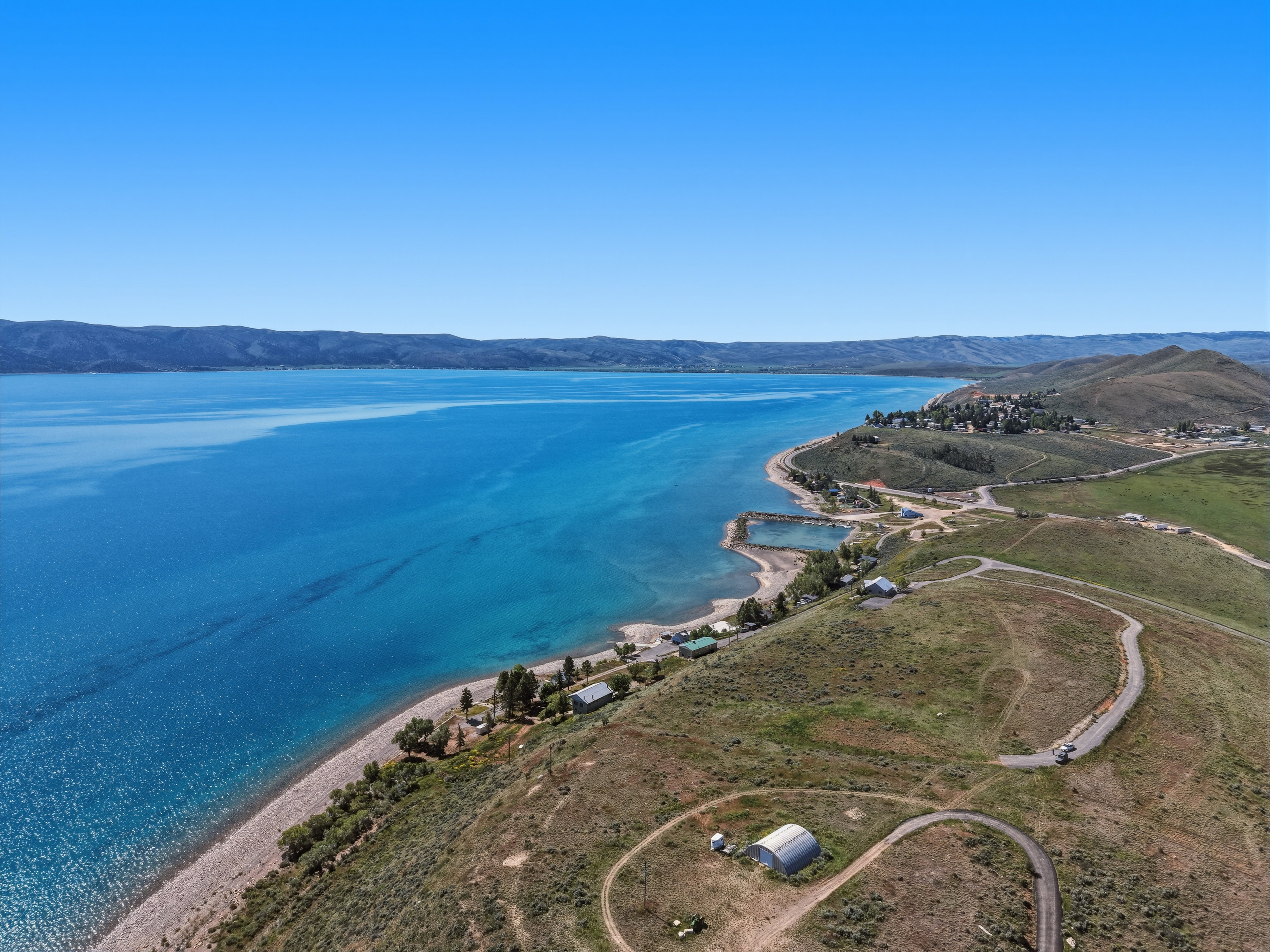 Expansive waterfront terrain with a clear blue lake, a rocky shoreline, and distant mountain ranges