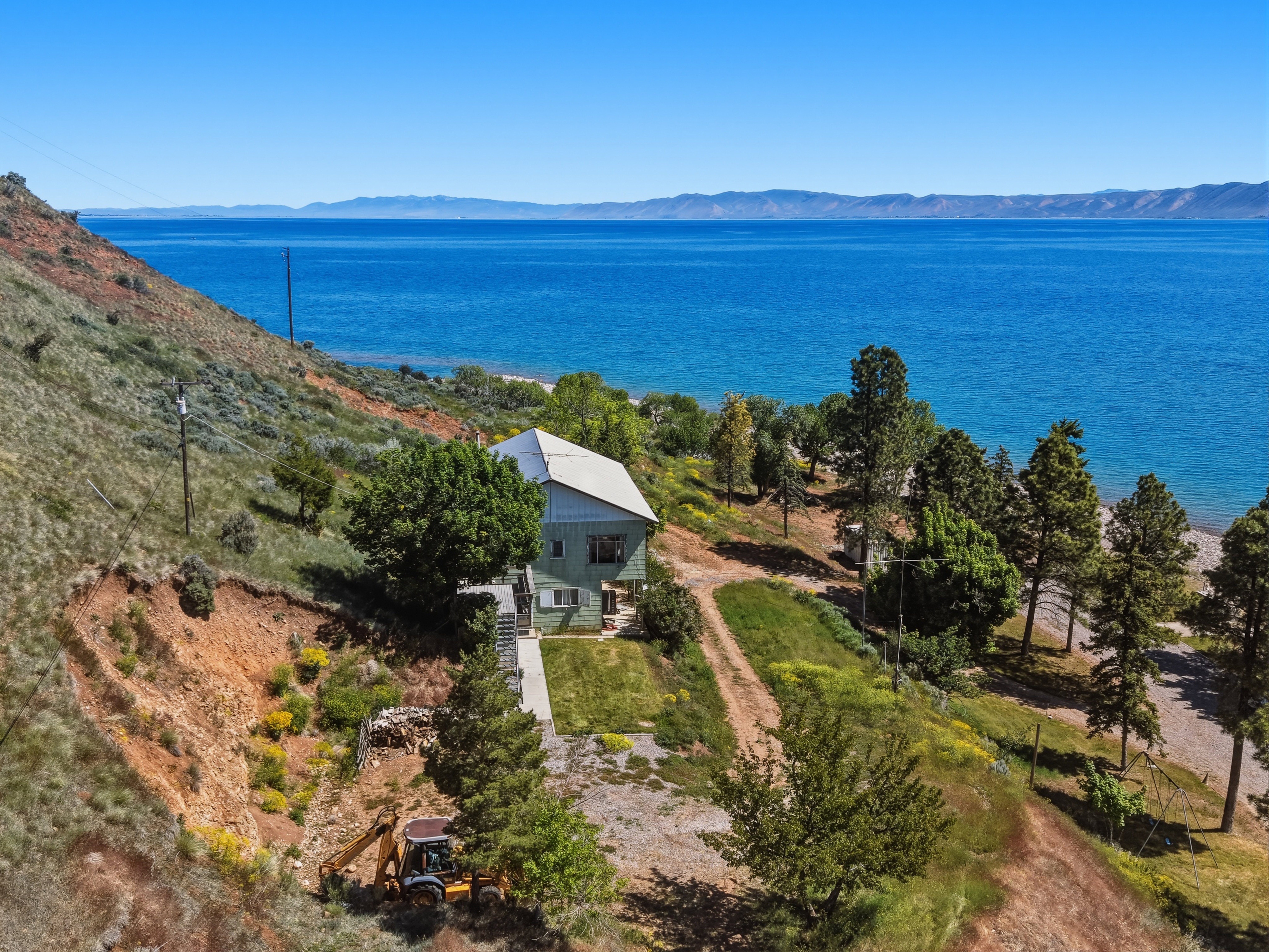 Lakefront property featuring a sloped, natural landscape and mature trees