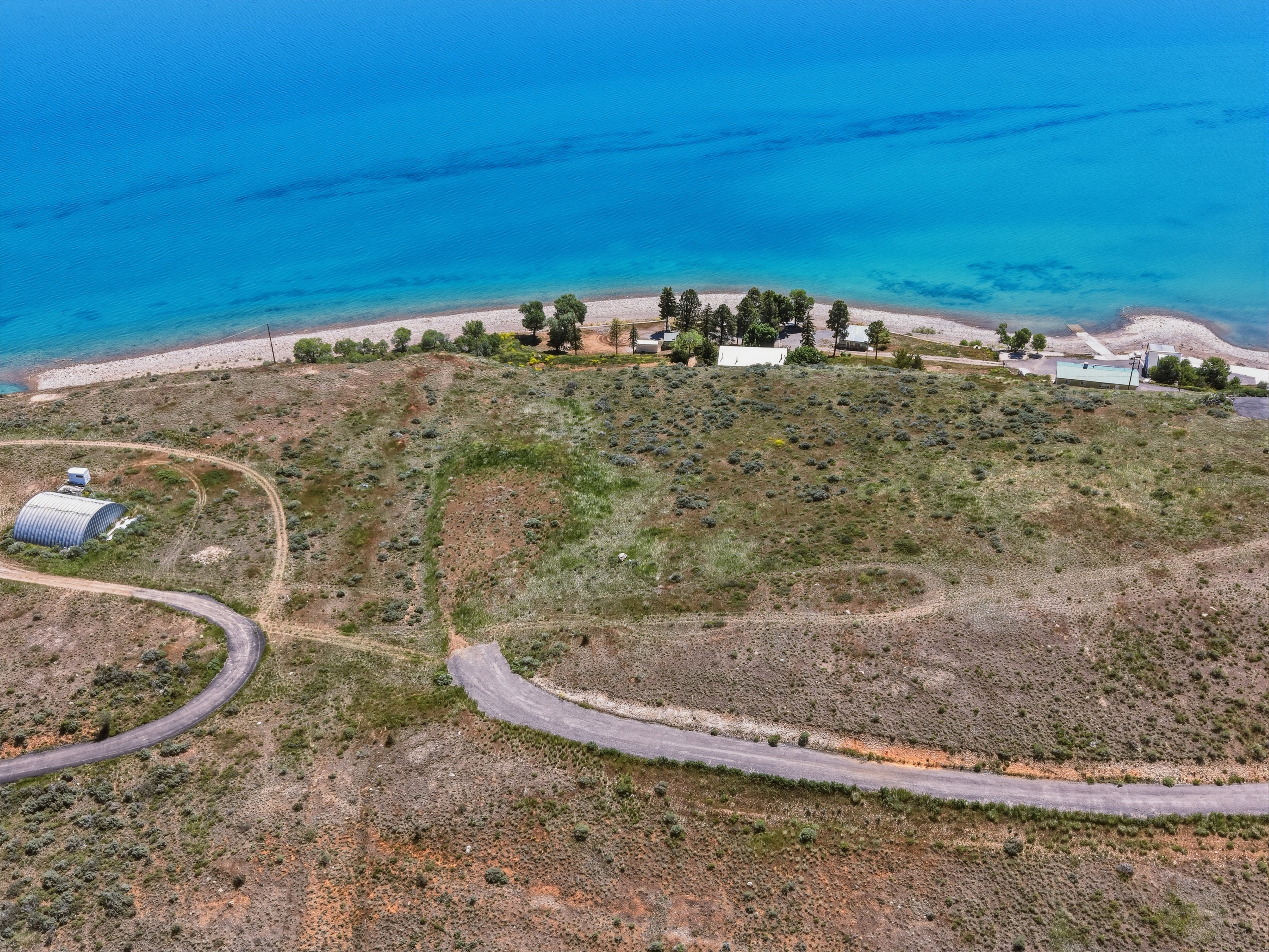 Expansive waterfront land featuring a private beach, multiple structures, and a paved access road