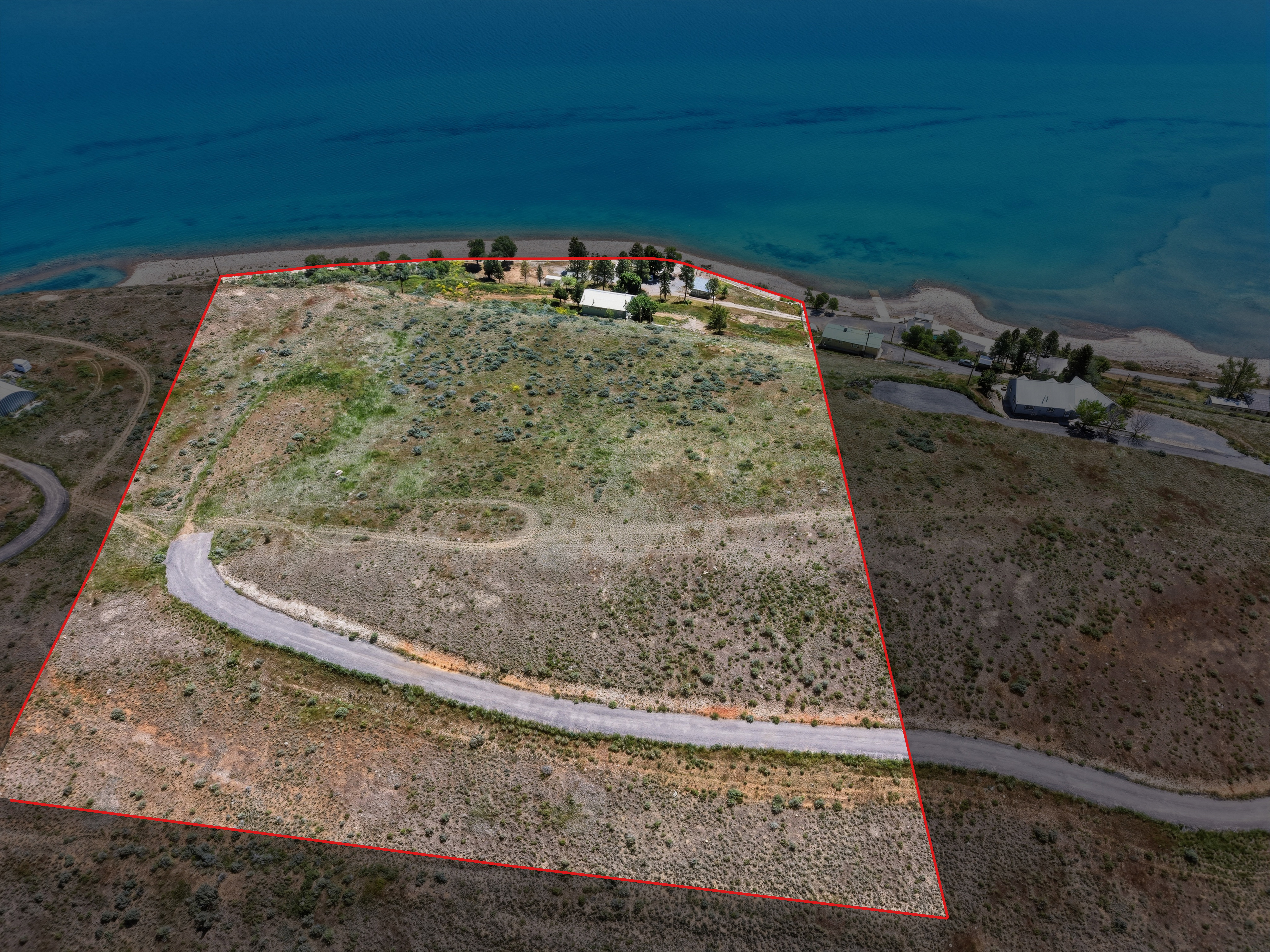 Expansive land parcel featuring a curved asphalt road, natural vegetation, and direct water frontage