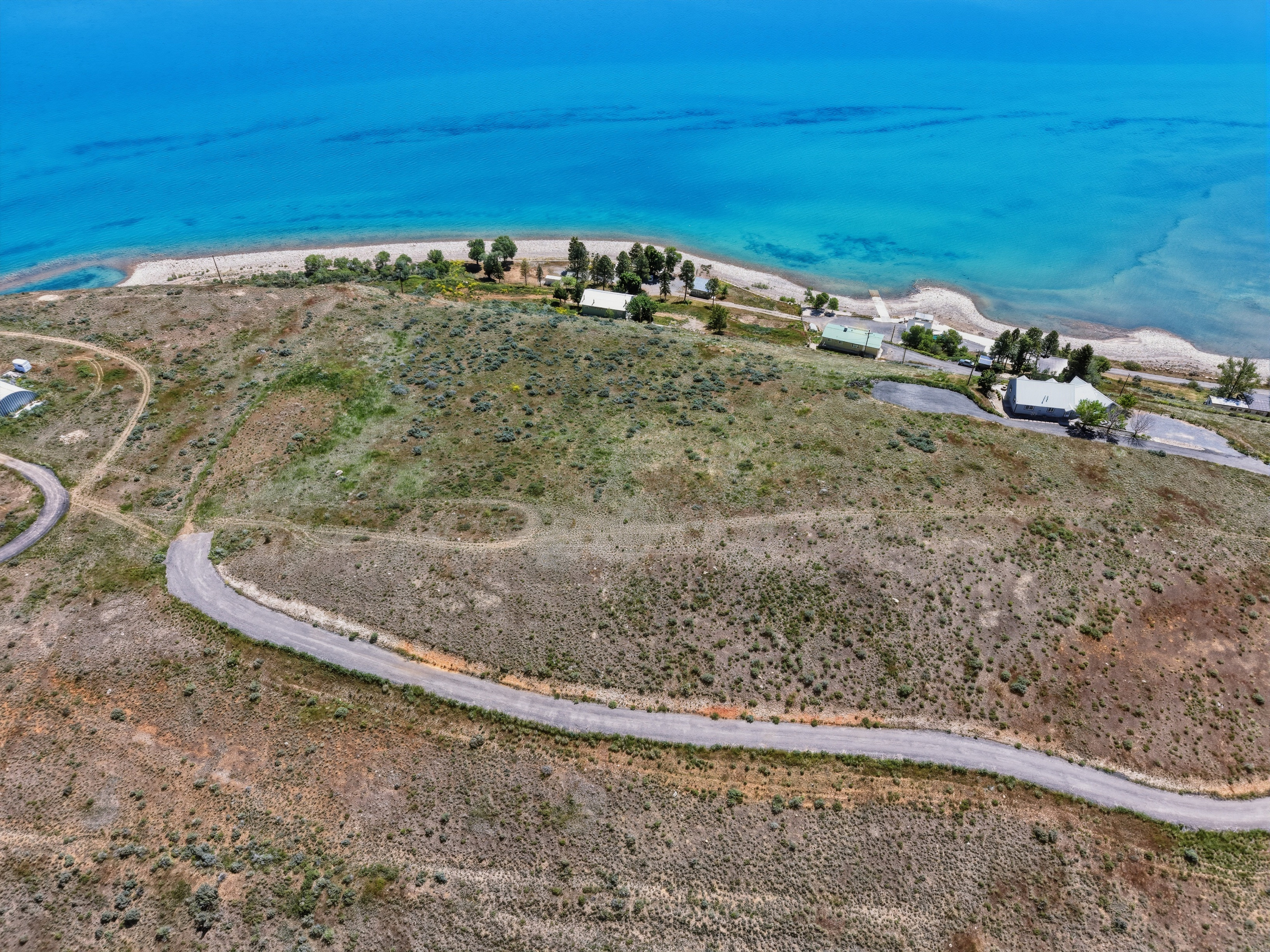 Expansive undeveloped land featuring a winding paved road, diverse ground cover, and direct waterfront access to a large body of water