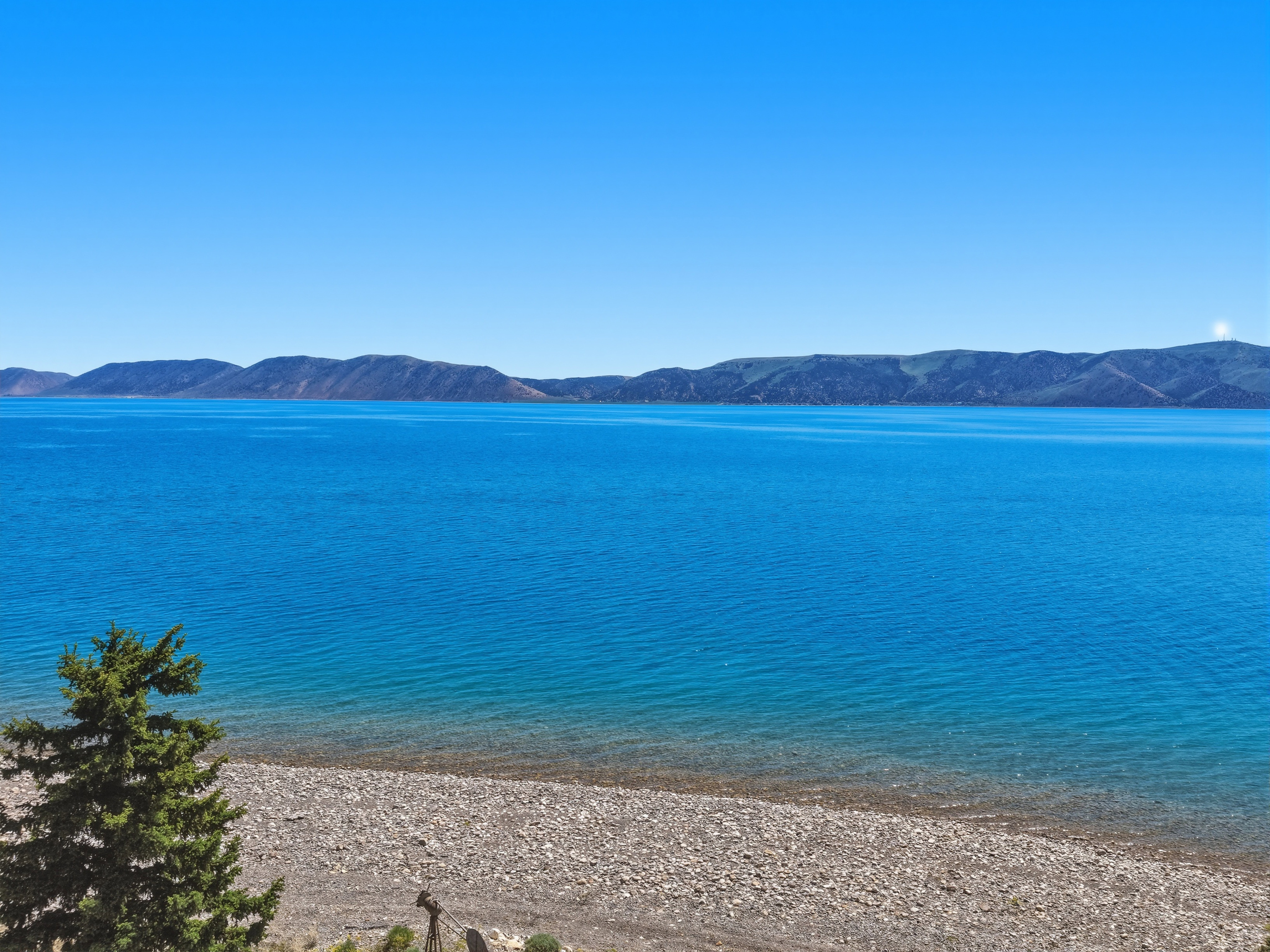 Expansive water body with a clear shoreline and distant mountains under a bright sky