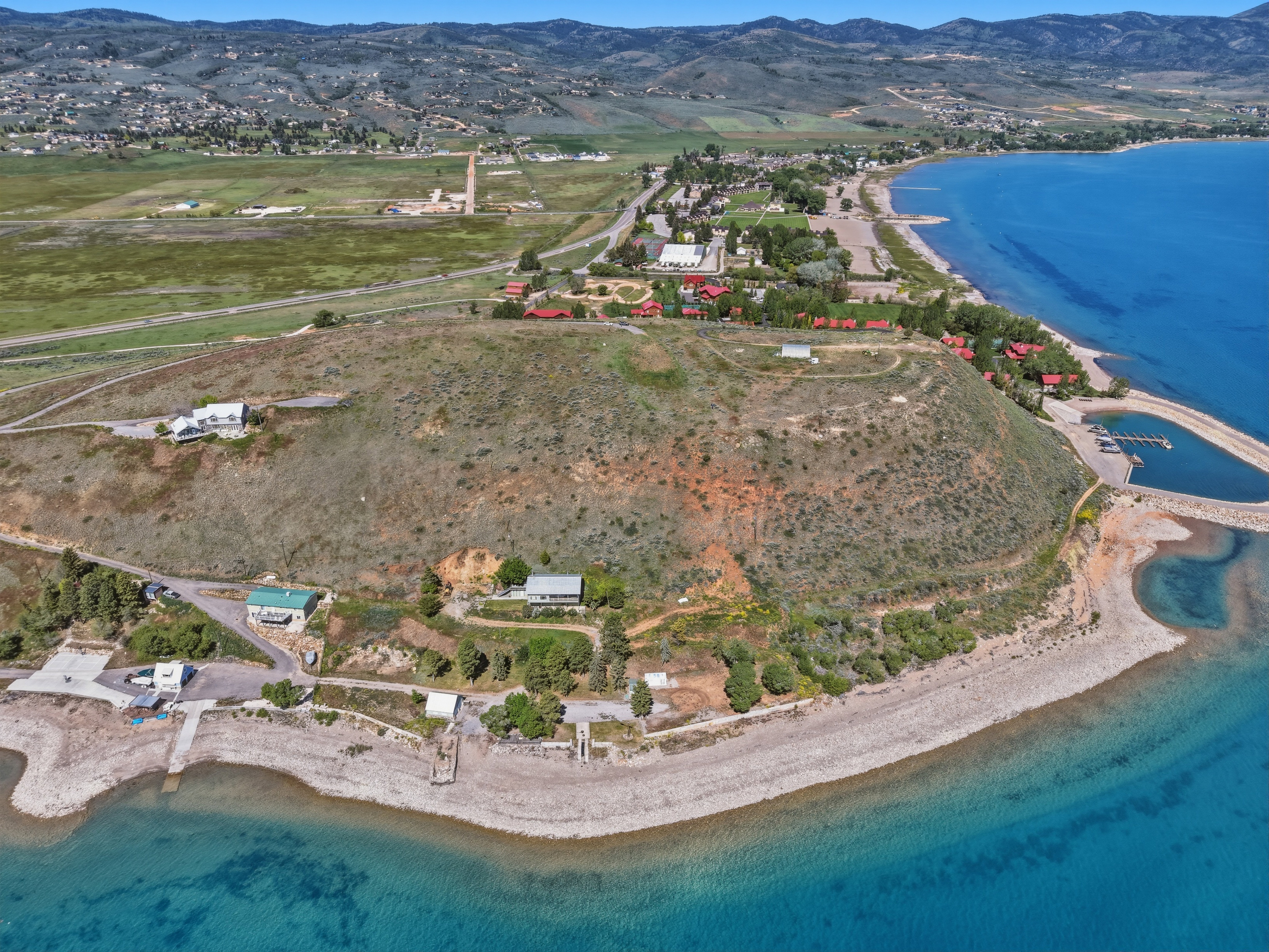 Expansive aerial showcasing a significant land parcel with diverse topography, featuring elevated building sites, waterfront access, a private dock, and surrounding natural landscape including a large body of water