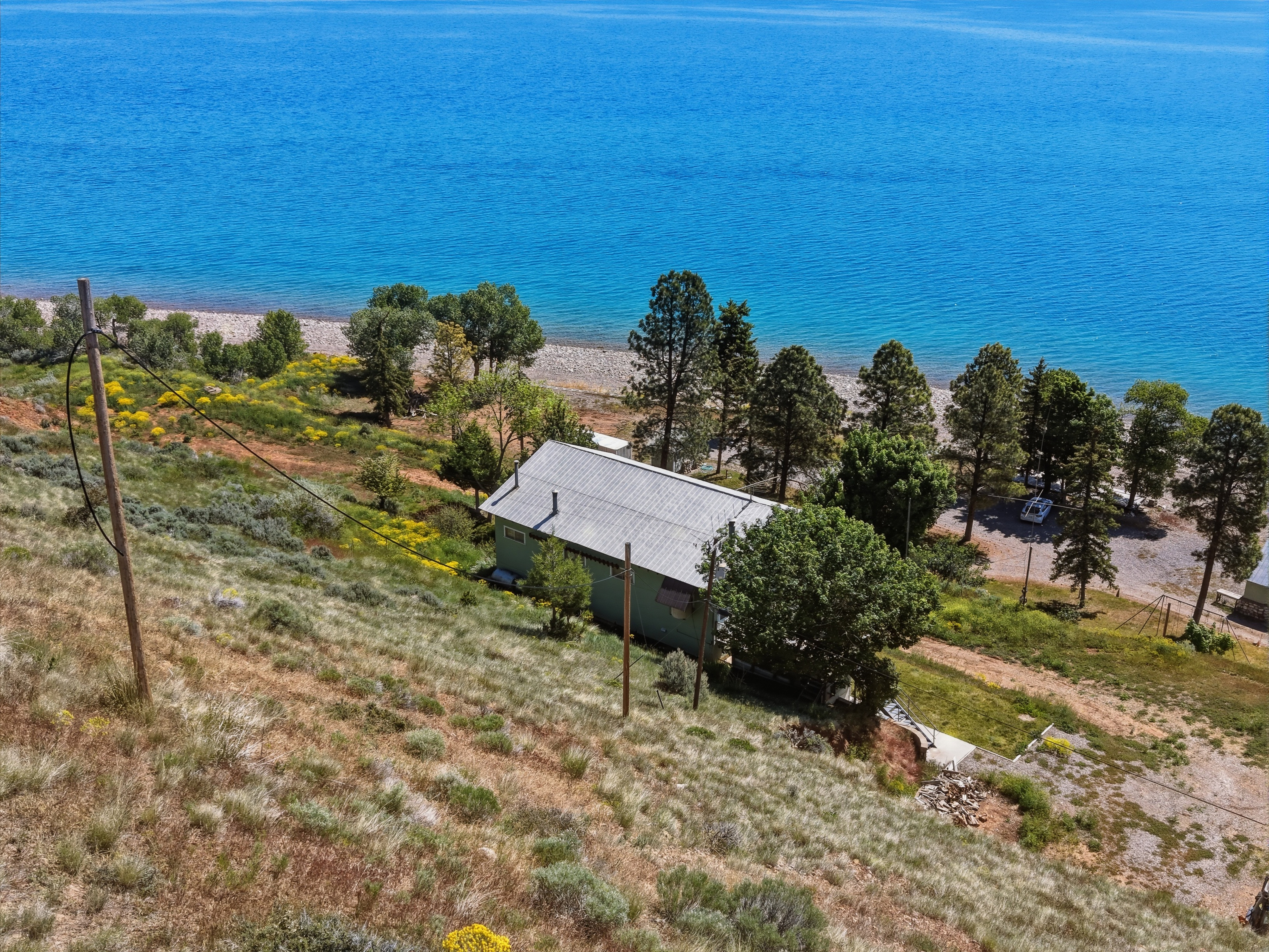 Waterfront property featuring a pitched roofline, mature trees, and a gravel shoreline