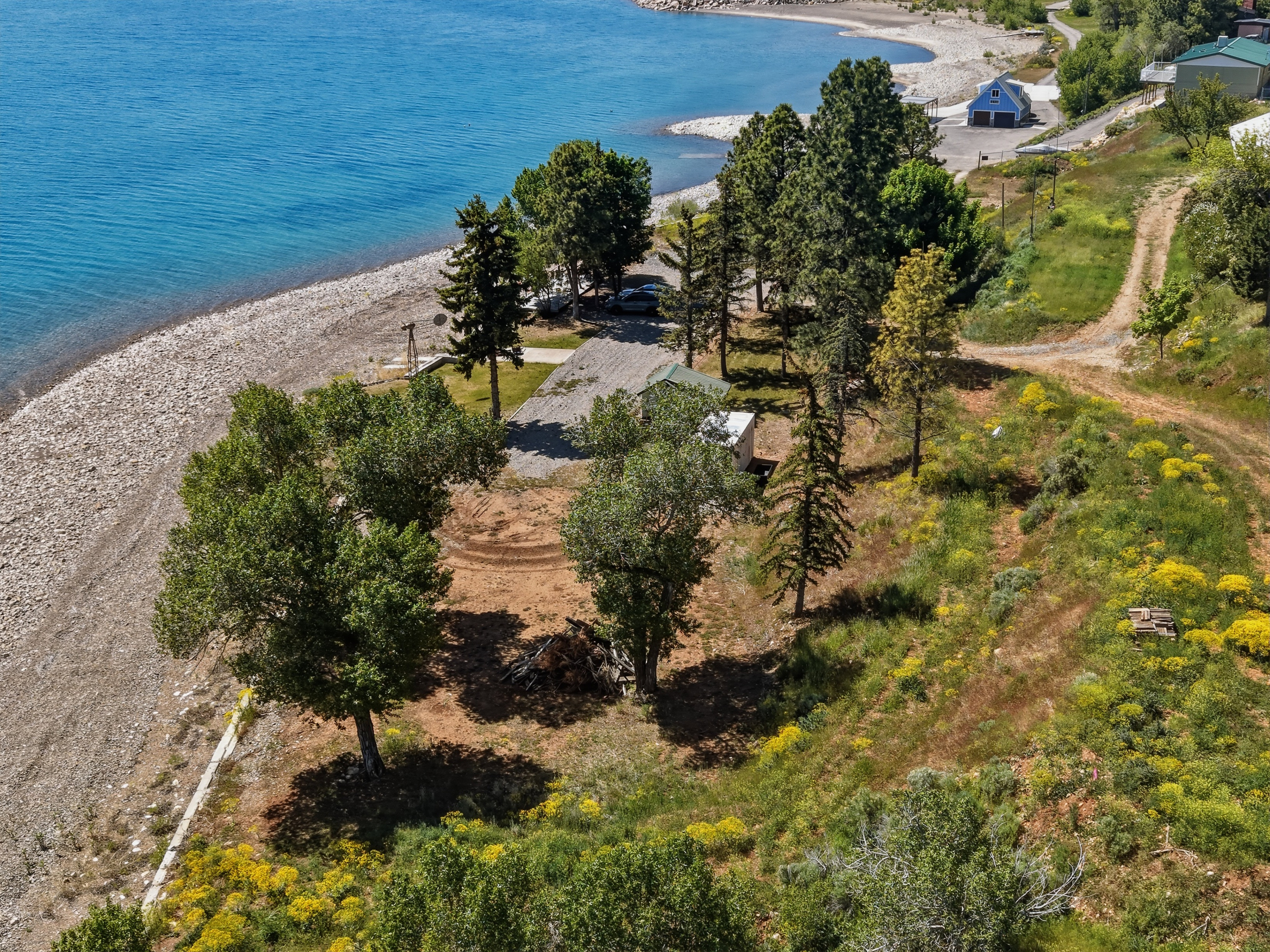 Expansive waterfront property featuring a gravel beach, mature trees, a partially cleared building site, and a natural hillside landscape