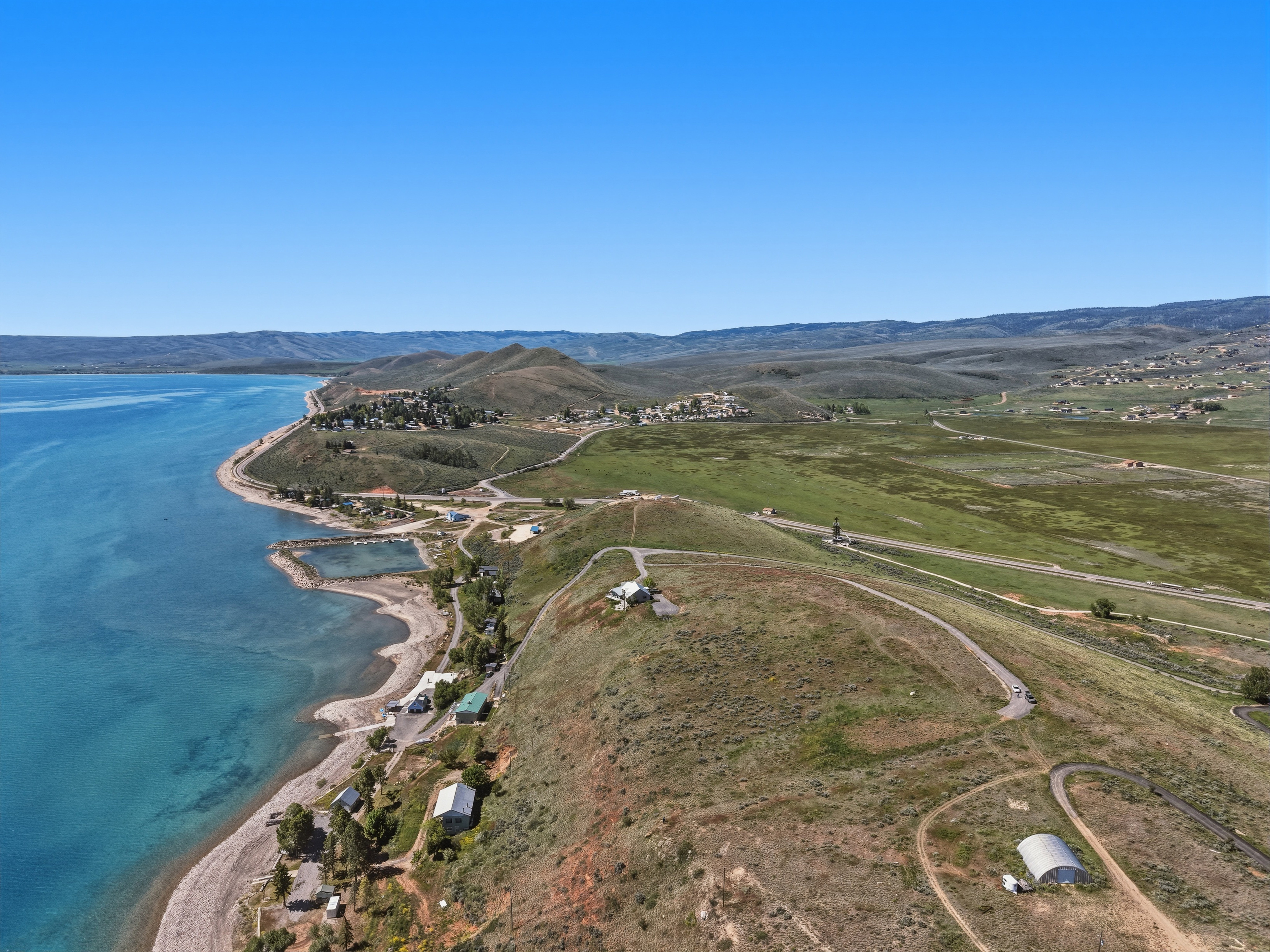 Expansive waterfront property featuring a large body of water, distant mountains, a natural shoreline, and scattered structures