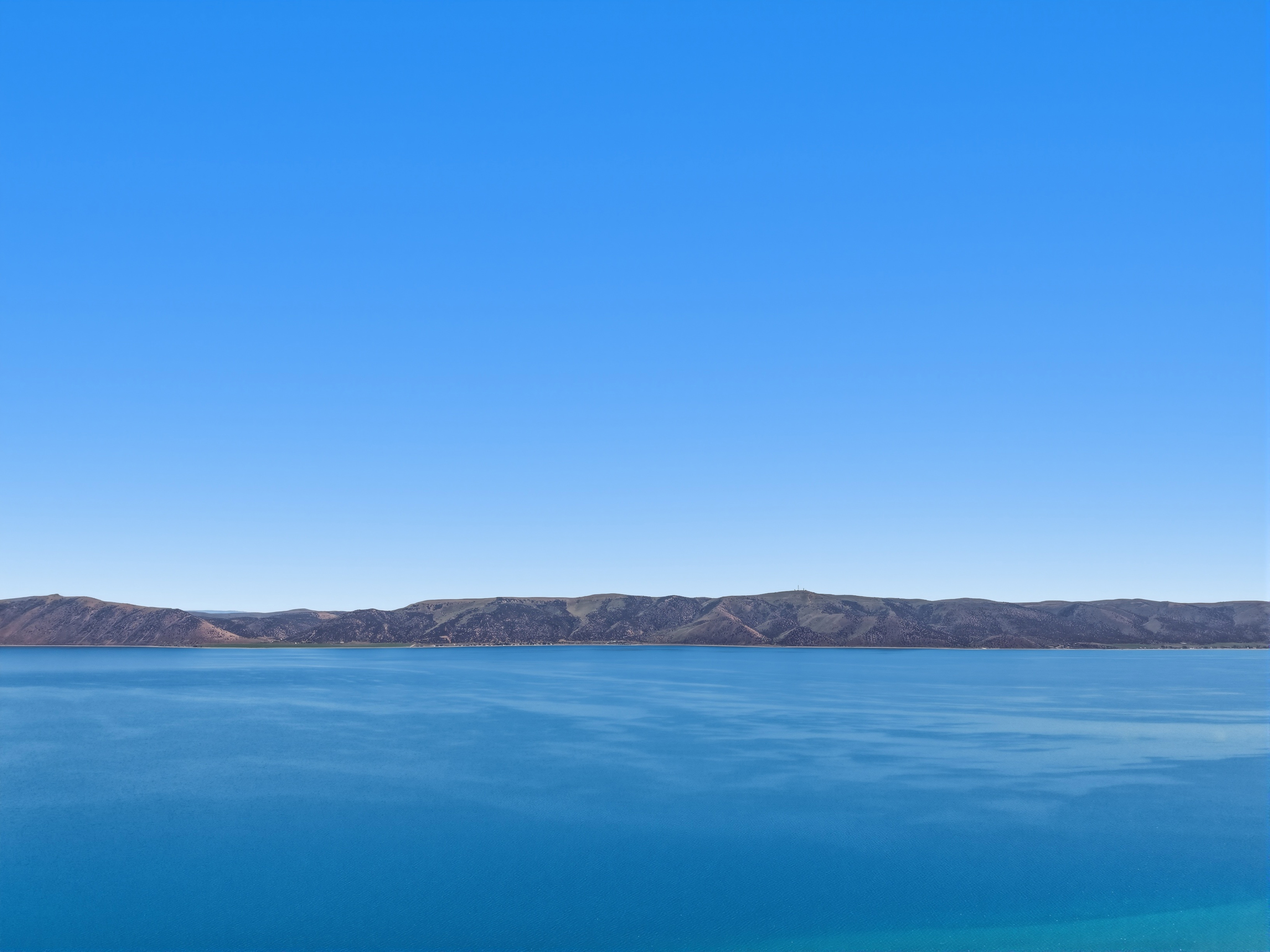 Expansive water body with distant mountainous terrain under a clear blue sky
