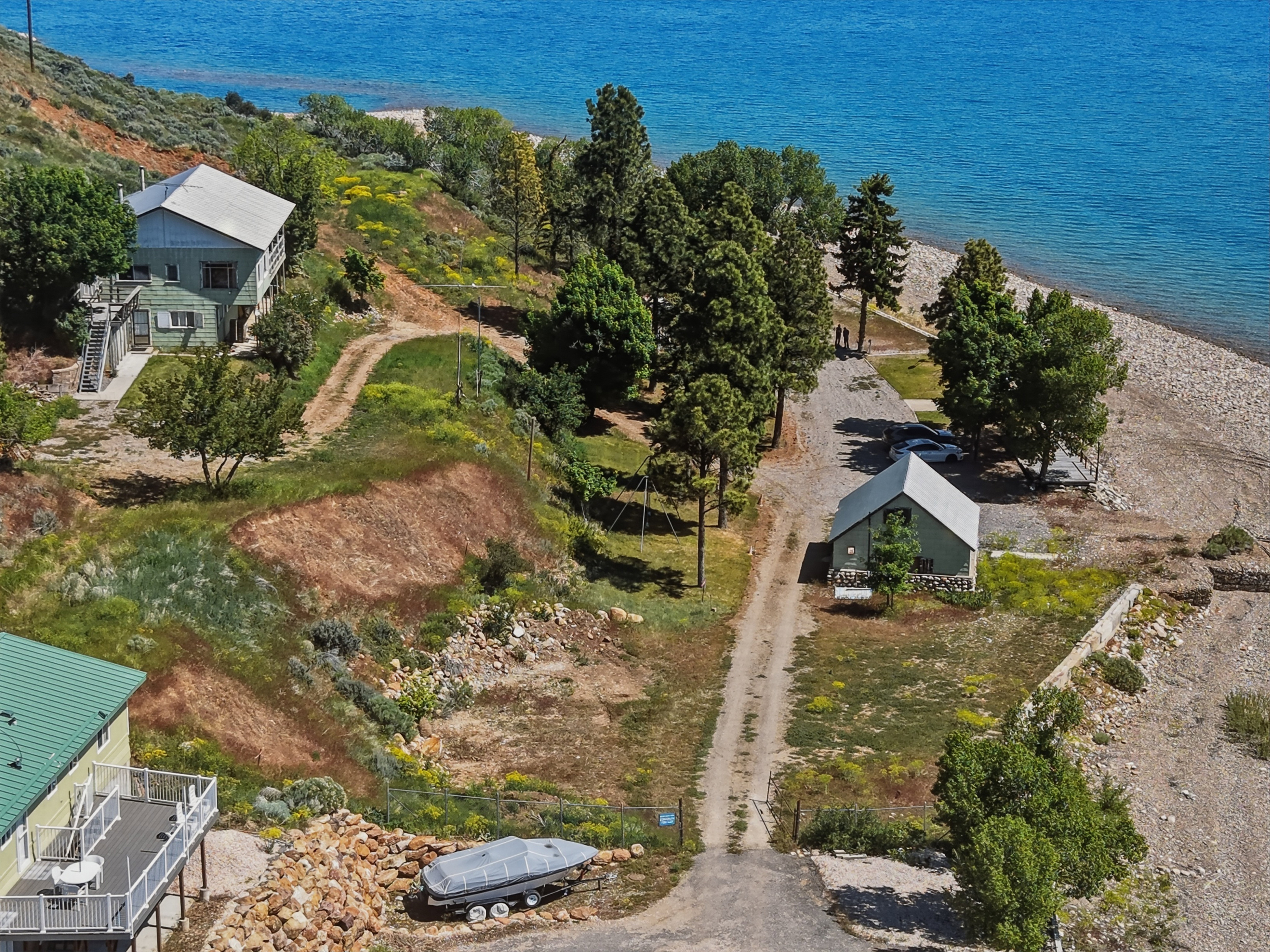 Waterfront property featuring three structures, mature trees, and direct access to a pebble beach