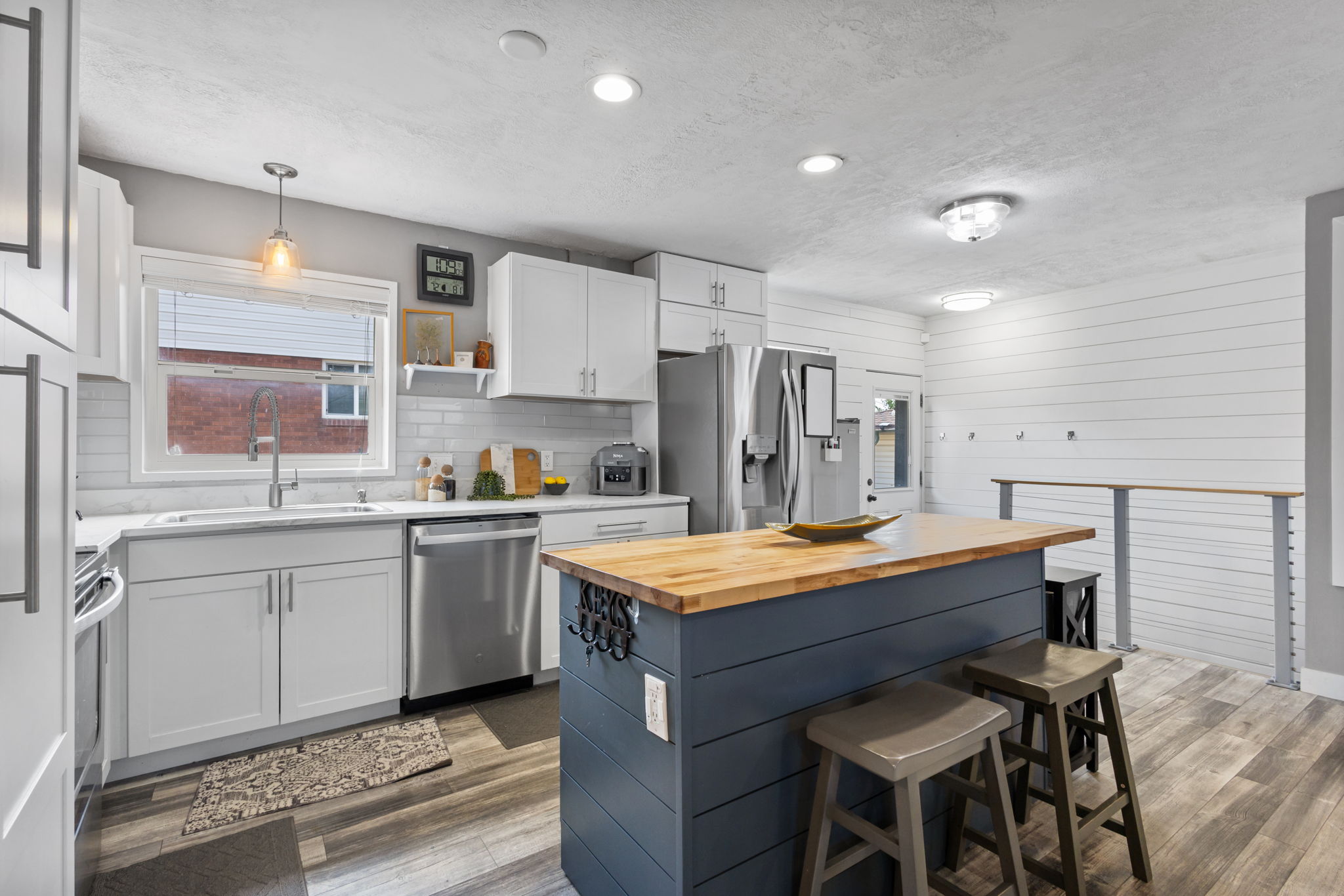 Contemporary kitchen featuring white shaker cabinetry, stainless steel appliances, a white subway tile backsplash, and a central island with a wood-finish countertop