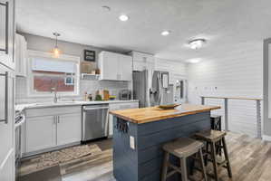 Contemporary kitchen featuring white shaker cabinetry, stainless steel appliances, a white subway tile backsplash, and a central island with a wood-finish countertop