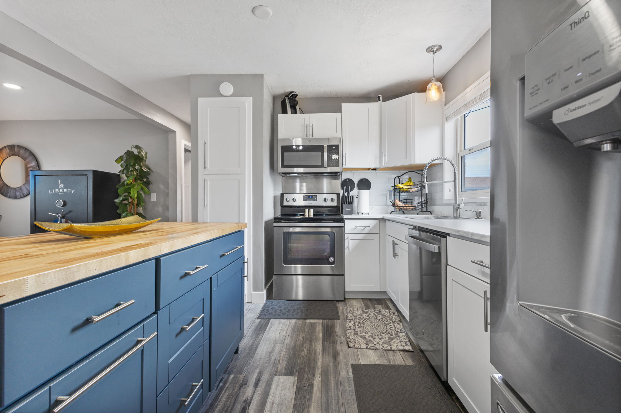 Kitchen featuring a blue-painted island with a wood countertop, white cabinetry, stainless steel appliances, and wood-finish flooring